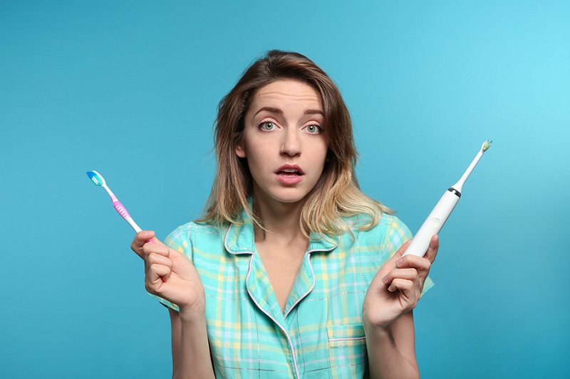Young Woman Choosing Between Manual And Electric Toothbrushes