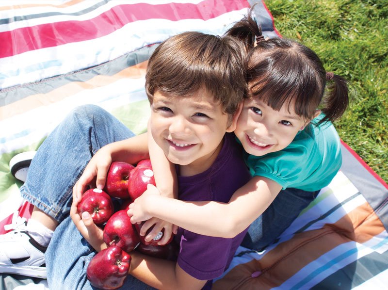 Ayoung boy and girl playing outside with apples.